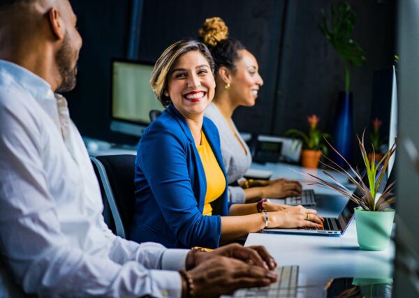 Team working on computers with a woman smiling in conversation