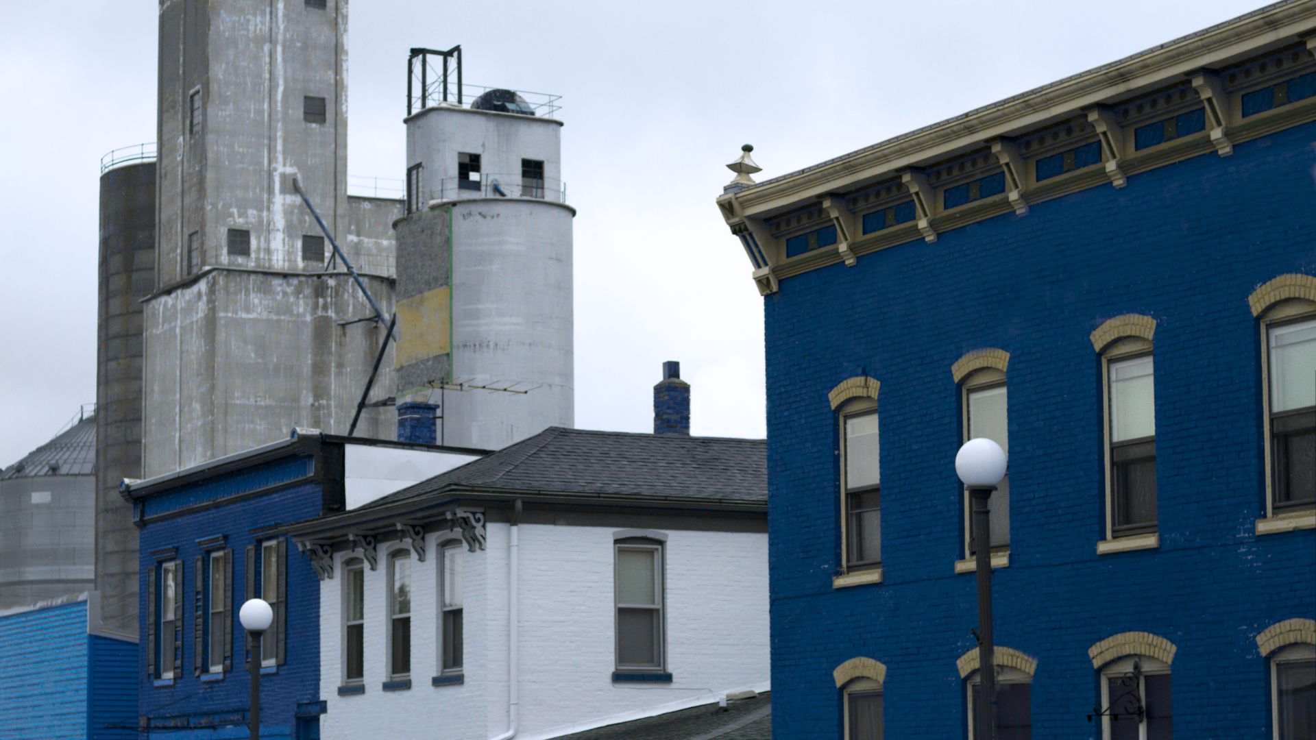 Street view of an industrial area with blue-painted historic buildings and concrete silos in the background